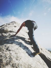 Low angle view of man climbing on mountain against sky