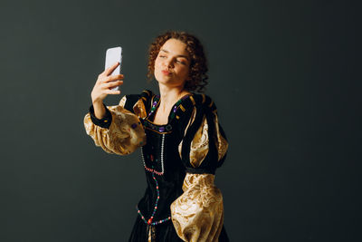 Portrait of young woman holding mobile phone against black background