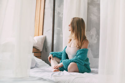 Full length of woman sitting on bed at home