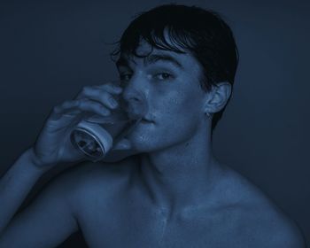 Portrait of a serious young man drinking water against blue background