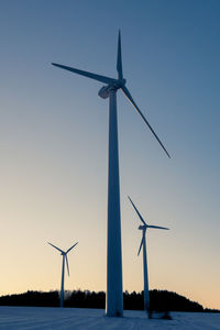 Low angle view of windmills against clear sky in winter