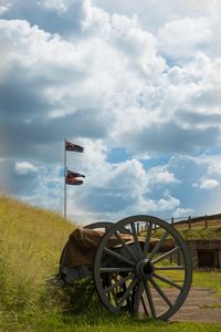 Cannon on field against cloudy sky