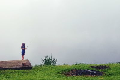 Woman standing on grass against clear sky