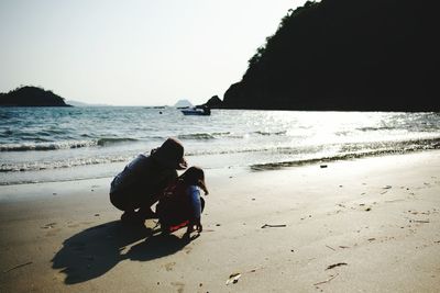 Rear view of people sitting on beach against clear sky