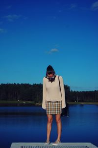 Woman standing by lake against blue sky