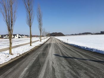 Snow covered road amidst field against clear sky