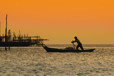 Silhouette of man in boat on sea during sunset