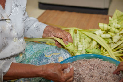 Hands of senior woman wrapping the sticky rice with palm leaf or ketupat palas