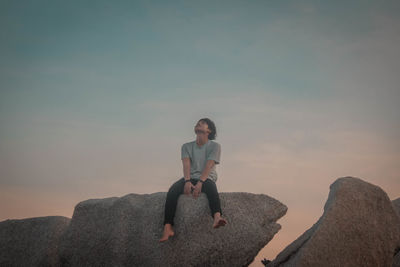 Full length of man sitting on rock against sky during sunset