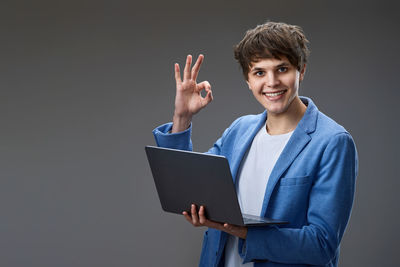 Portrait of young businesswoman using laptop while standing against white background