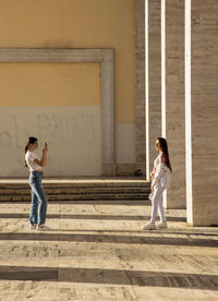 Full length of young woman standing against building