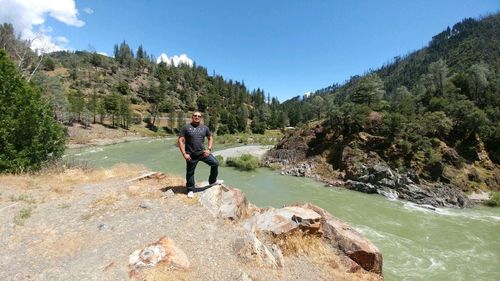 Man standing on cliff by river against sky