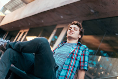 Low angle portrait of man smiling while sitting on seat against building