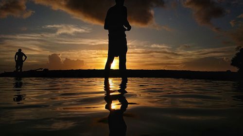 Silhouette people standing on shore against sky during sunset