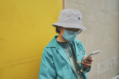Full length of man holding mobile phone while standing against yellow wall