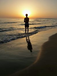 Silhouette man standing on beach against sky during sunset