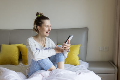 Young woman using mobile phone while lying on bed at home