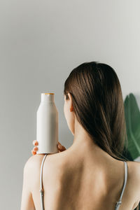 Woman holds a white bottle of cosmetics in her hand, standing with her back to the camera. mock up 