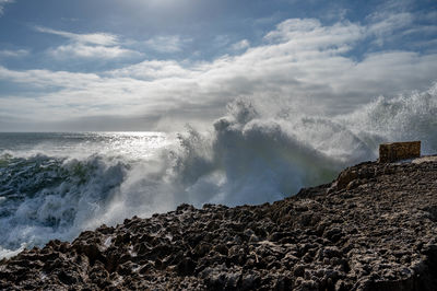 Waves splashing on rocks at shore against sky