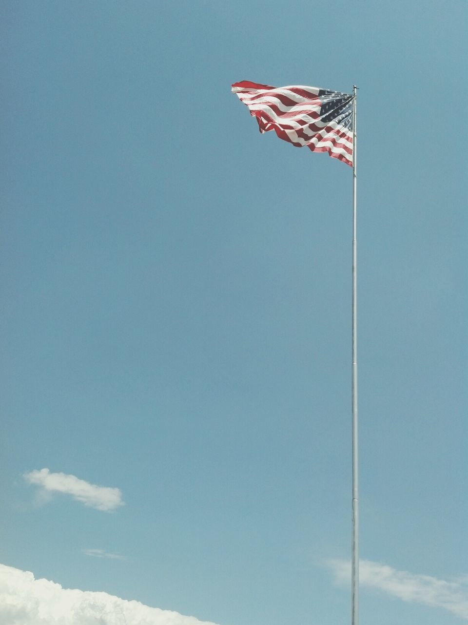 flag, patriotism, national flag, identity, american flag, low angle view, clear sky, wind, blue, pole, culture, striped, copy space, sky, red, pride, day, flag pole, no people, outdoors