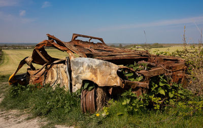 Old rusty wheel on field against sky