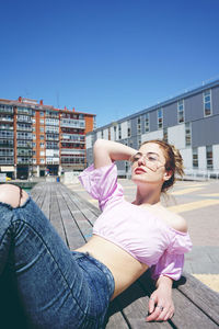 Young woman resting on bench against buildings in city