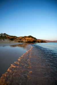 Surface level of beach against clear blue sky