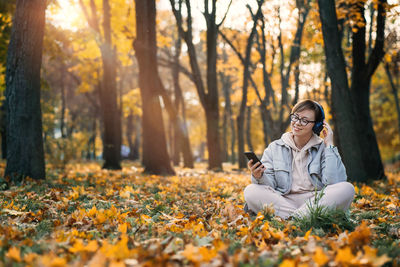 Caucasian middle aged woman in earphones listening to music, meditation app on smartphone and