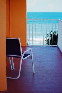 Empty chairs on table by sea against sky