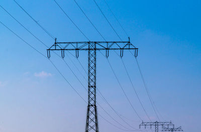 Low angle view of electricity pylon against clear blue sky