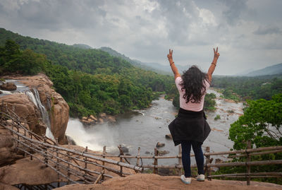 Girl solo traveler at waterfall with cloudy sky and green forests of the western ghat range
