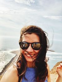 Portrait of young woman wearing sunglasses at beach against sky