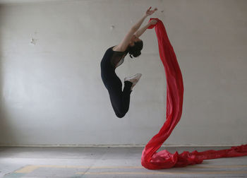 Side view of young woman doing ballet dance with red fabric