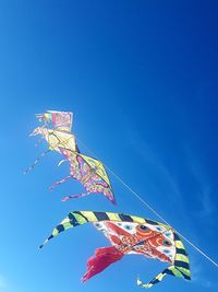 Low angle view of kites against clear blue sky