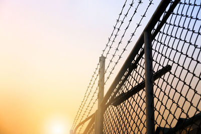 Low angle view of fence against sky during sunset