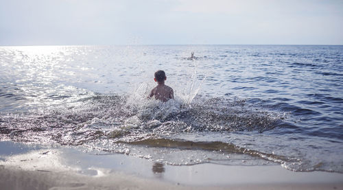 Happy sibling running into the sea and splashing in sunset light, lots of fun and happiness, summer 