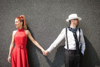 Young couple holding hands against wall while looking away