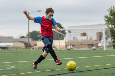 Full length of a boy playing soccer wearing face mask