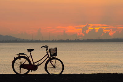 Bicycle by lake against sky during sunset