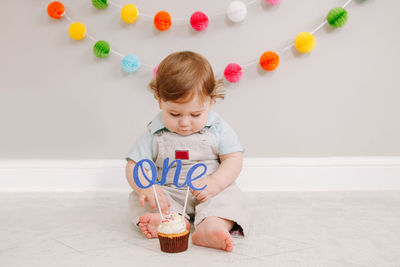 Cute baby boy sitting by cake at home