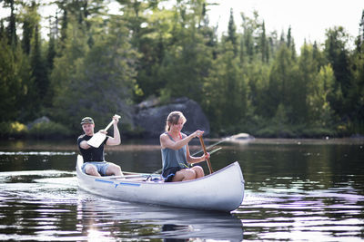 Friends canoeing on lake against trees