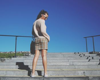 Low angle view of woman standing on steps against clear blue sky