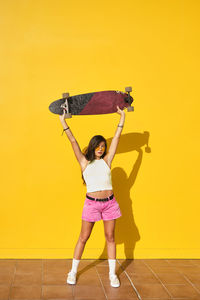 Full length portrait of smiling woman standing against yellow wall