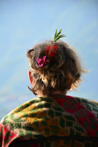 Rear view of woman with flowers in hair against sky