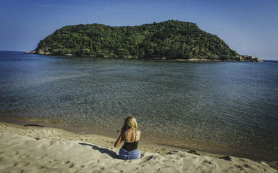 Rear view of woman on beach against clear sky