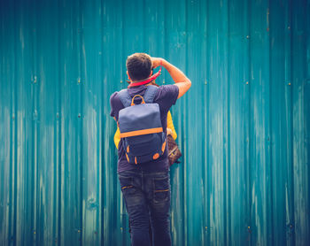 Rear view of man photographing against blue wall