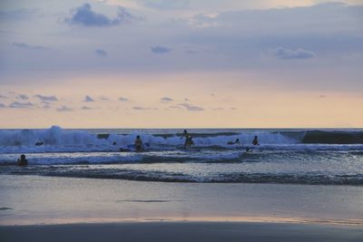 People surfing in sea against sky during sunset