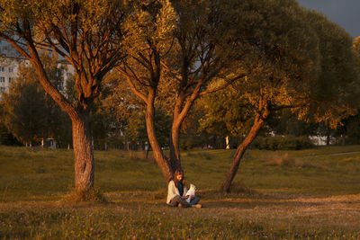 Young woman with white dog siting in autumn park at sunset. concept of tranquility and conciliation.