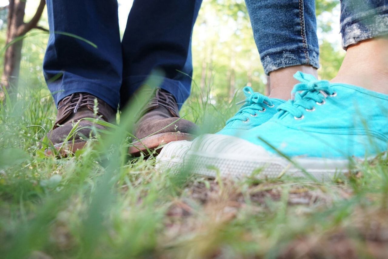 low section, person, lifestyles, leisure activity, men, shoe, standing, human foot, togetherness, grass, jeans, casual clothing, field, bonding, selective focus