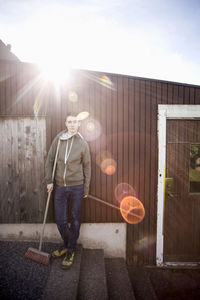 Portrait of confident teenage boy holding broom outside house